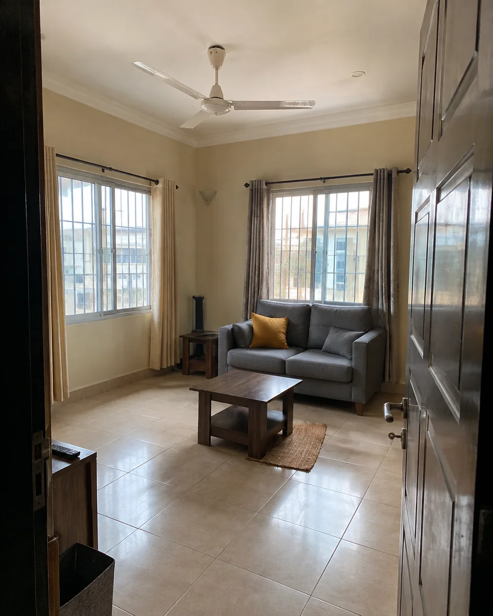 A tidy living room with a grey sofa and clean tiled floor